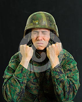 Handsome young soldier wearing uniform suffering from stress, pucker his face with both hands doing fist, in a black