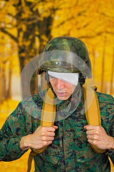 Handsome young soldier wearing uniform suffering from stress, with a white bandage around his head and covering his eye