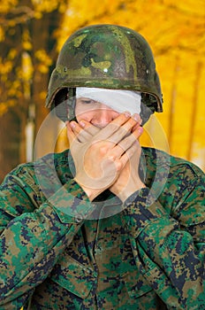 Handsome young soldier wearing uniform suffering from stress, with a white bandage around his head and covering his eye