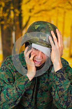 Handsome young soldier wearing uniform suffering from stress, with a white bandage around his head and covering his eye