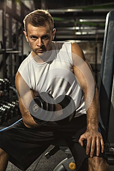 Handsome young sportsman exercising with dumbbells at the gym