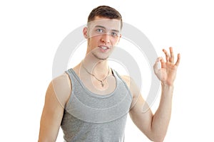 Handsome young sporty guy looks into the camera and shows the gesture Okey isolated on a white background