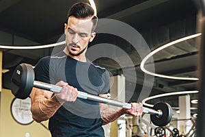 Handsome young sporty male bodybuilder doing barbell exercise in gym