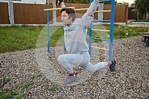 Handsome young sporty man in active wear exercising outdoor with suspensions straps, doing lunges. Bodyweight training