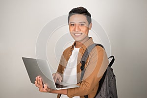 A handsome young student using laptop and carrying backpack isolated on white background