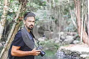 Handsome young stylish male photographer in black t-shirt and sunglasses is engaged in trekking in the green jungle