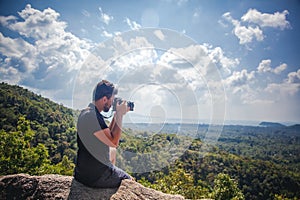 Handsome young stylish male photographer of mixed race in a black T-shirt with a camera in hand on top of a mountain with a view