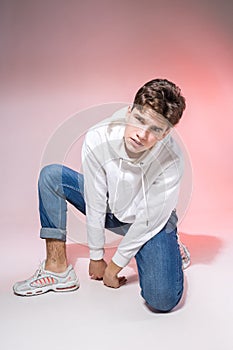 Handsome young stylish man sitting on the floor in studio. Teenager model posing while sitting on a pink background in casual