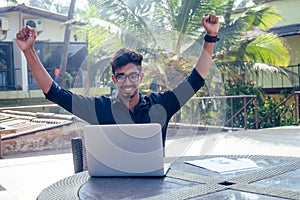 Handsome and young successful indian man freelancing surfing remote work with a laptop on the beach by the ocean.india
