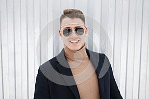 Handsome young successful male businessman with charming smile in stylish sunglasses in an expensive elegant coat