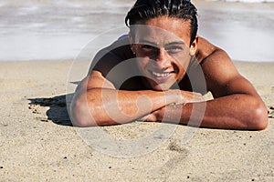 Handsome young teenager boy smile lay down on the sand at the beach with shore sea in background - student enjoying summer holiday