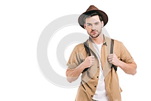 handsome young traveler in hat holding backpack and looking at camera