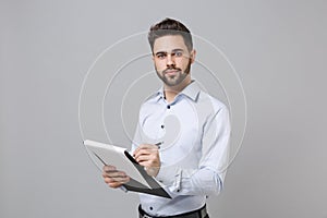 Handsome young unshaven business man in light shirt posing isolated on grey background. Achievement career wealth