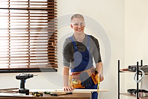 Handsome young working man using hand saw indoors