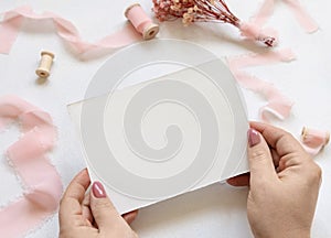 Hands with blank card near pink flowers and ribbons photo
