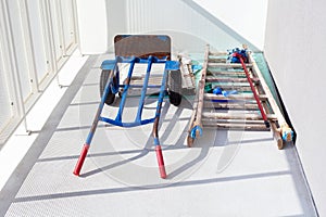 Handtruck and a wooden painter ladder and a mop laying on the white balcony. House or flat under construction abstract concept