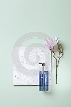 Handwash lotion on grey concrete podium and pale green background with magnolia flower, top view flat lay. Minimalistic