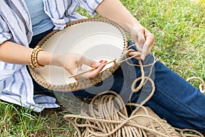 Handwork hobby Woman is crocheting a basket from a thick cord from eco friendly materials and wood bottom, on the grass