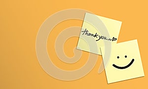 Handwriting of message thank you, heart shape and smile face on yellow sticky note on yellow background