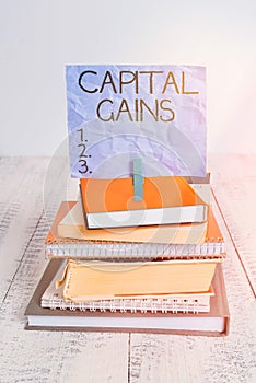 Handwriting text Capital Gains. Concept meaning Bonds Shares Stocks Profit Income Tax Investment Funds pile stacked books notebook