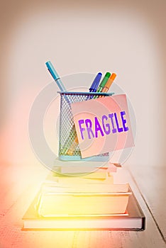 Handwriting text Fragile. Concept meaning Breakable Handle with Care Bubble Wrap Glass Hazardous Goods Stacked books pens metal