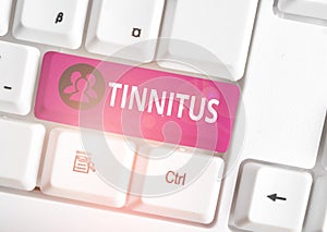 Handwriting text Tinnitus. Concept meaning A ringing or music and similar sensation of sound in ears White pc keyboard
