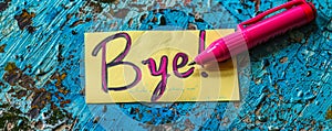 Handwritten Bye! farewell message on a yellow sticky note with pink marker, symbolizing parting, goodbyes, end of