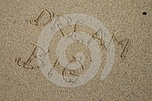 Handwritten DREAM BIG on a sandy sea beach on a summer sunny day. Disappearing dreams concept