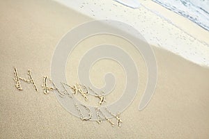 handwritten inscription happy day made in the sand near the water, the wave washes text on the beach