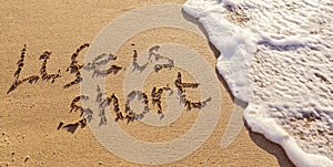 Handwritten inscription Life is Short on the sand with flushing foamy wave