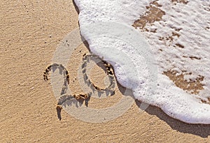 Handwritten inscription 20 on the sand with foamy wave