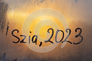 lettering Szia in Hungarian is hello in english and numbers 2023 of new year paint with finger on splashed by rain foggy photo