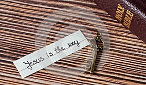 A handwritten text with a rustic vintage old key and closed Holy Bible Book on a wooden table.