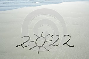 2022  handwritten text and a sun drawn in sand on a beach with waves in an exotic island for unity photo