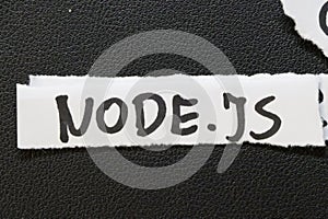 Handwritten text on a torn paper strip displaying NODE.JS. Node.js is a JavaScript runtime built on Chromes V8 engine, c