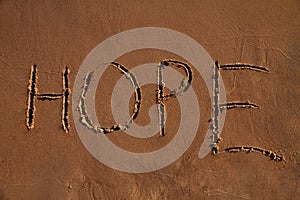 Handwritten word Hope on wet yellow sand on beach