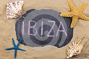 Handwritten word IBIZA written in chalk, among seashells and starfishes