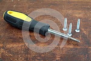 Handy screw driver and three sharp screws on brown wooden background closeup view