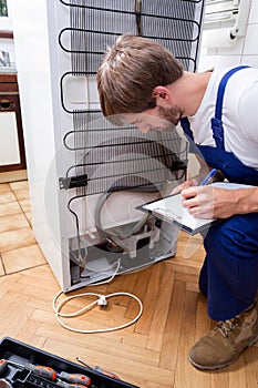 Handyman bends down, looks at the fridge