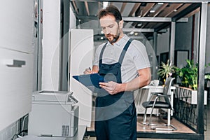 Handyman checking copy machine and writing in clipboard photo