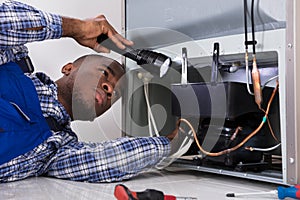 Handyman Checking Refrigerator With Flashlight