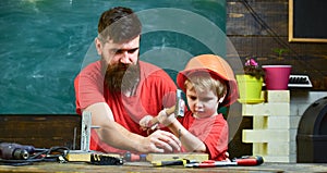 Handyman concept. Boy, child busy in protective helmet learning to use hammer with dad. Father with beard teaching