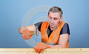 Handyman concept. Man, handyman in working uniform and protective gloves handcrafting with hammer, light blue background