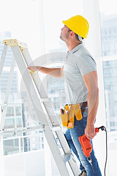Handyman with drill machine climbing ladder in building