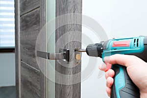 Handyman Fitting A New Door Using A Screwdriver At Home. Carpenter at lock installation with electric drill into interior wood