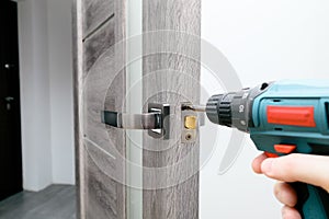 Handyman Fitting A New Door Using A Screwdriver At Home. Carpenter at lock installation with electric drill into interior wood