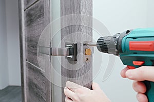 Handyman Fitting A New Door Using A Screwdriver At Home. Carpenter at lock installation with electric drill into interior wood