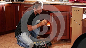 Handyman fixing cabinet with screwdriver in kitchen