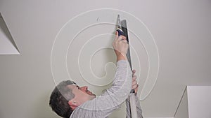 Handyman with handsaw making drywall ceiling holes for lighting installation