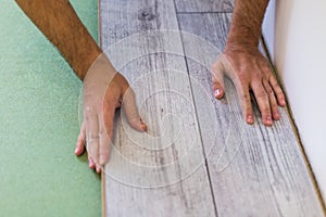 Handyman laying down laminate flooring boards while renovating a house. hands closeup